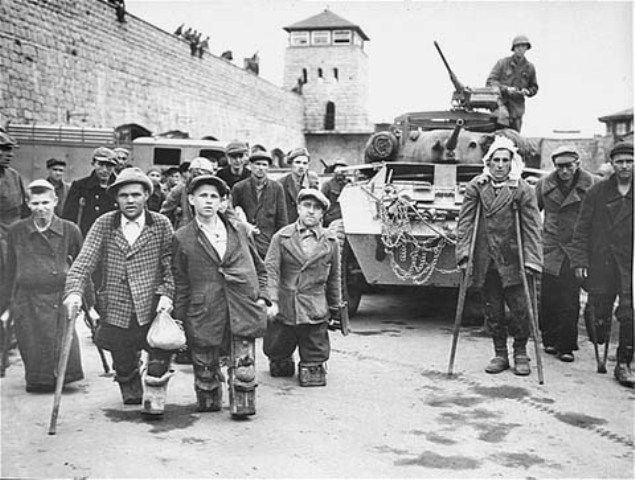 Disabled Polish and Russian survivors stand in front of a tank from the US 11th Armored Division